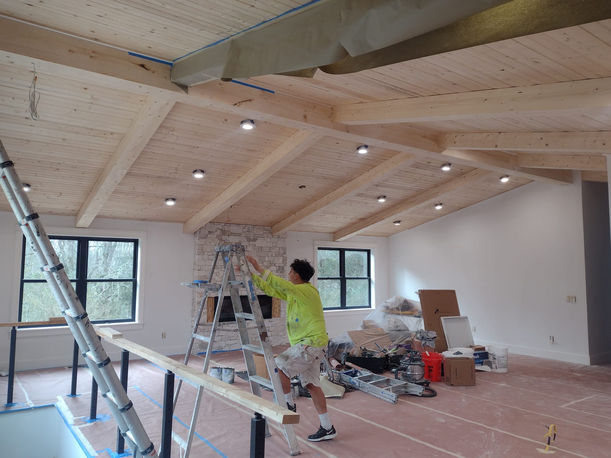 Interior painting — worker on ladder painting room with exposed beam ceiling in Nashville home